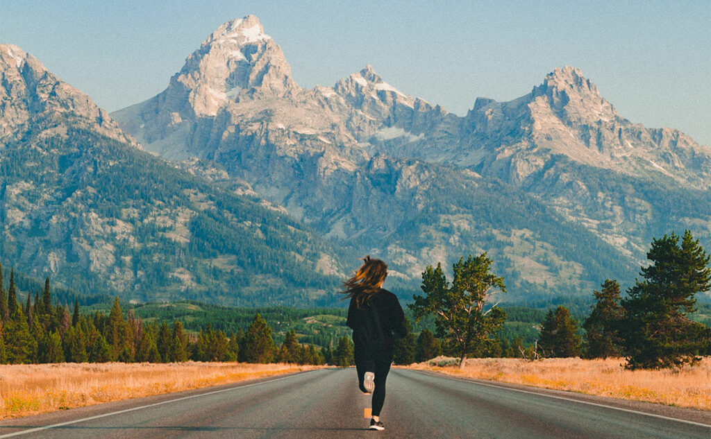 Woman running on the road towards the mountains with positive Monday blessings quotes